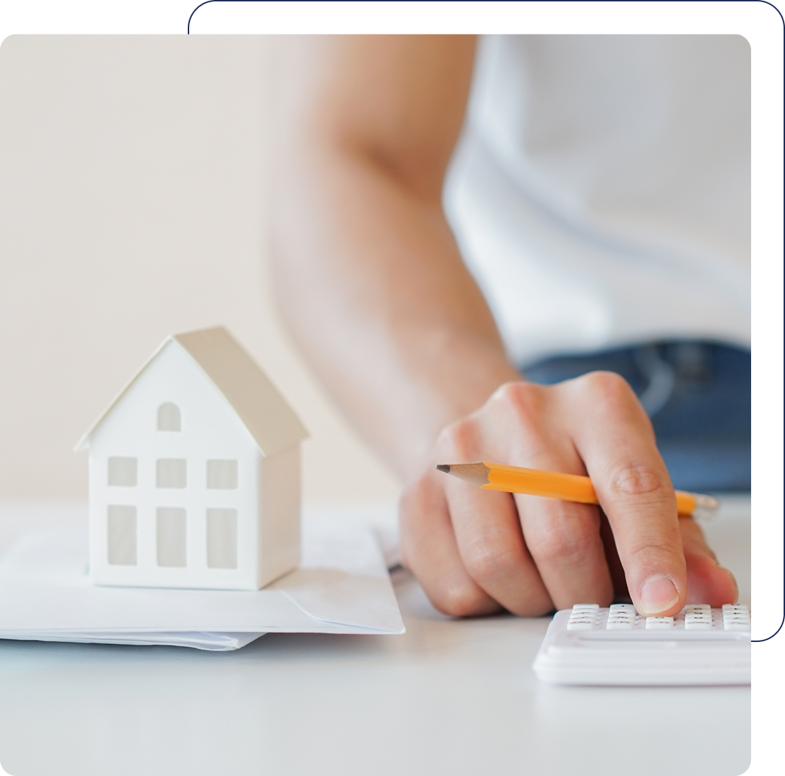 Person calculating with house model nearby.