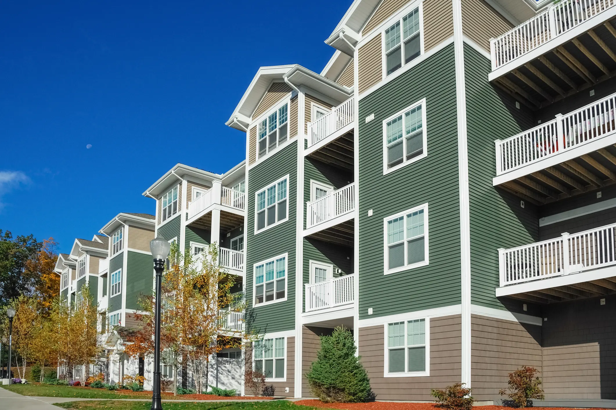 Modern green apartment buildings with balconies under a clear blue sky.